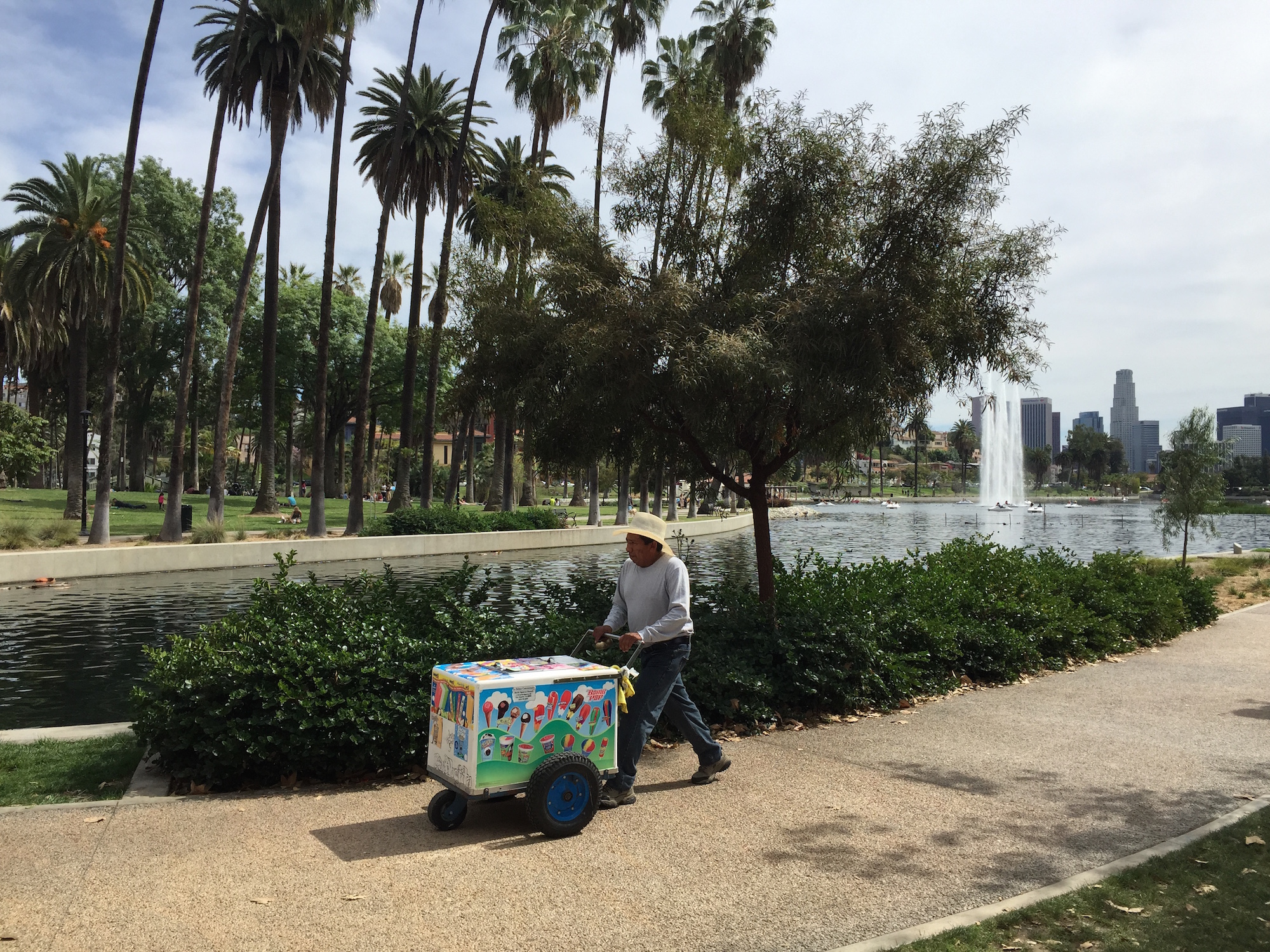 A street food vendor in the summer pushes a cart along a sandy path near a park lake in 2019.
