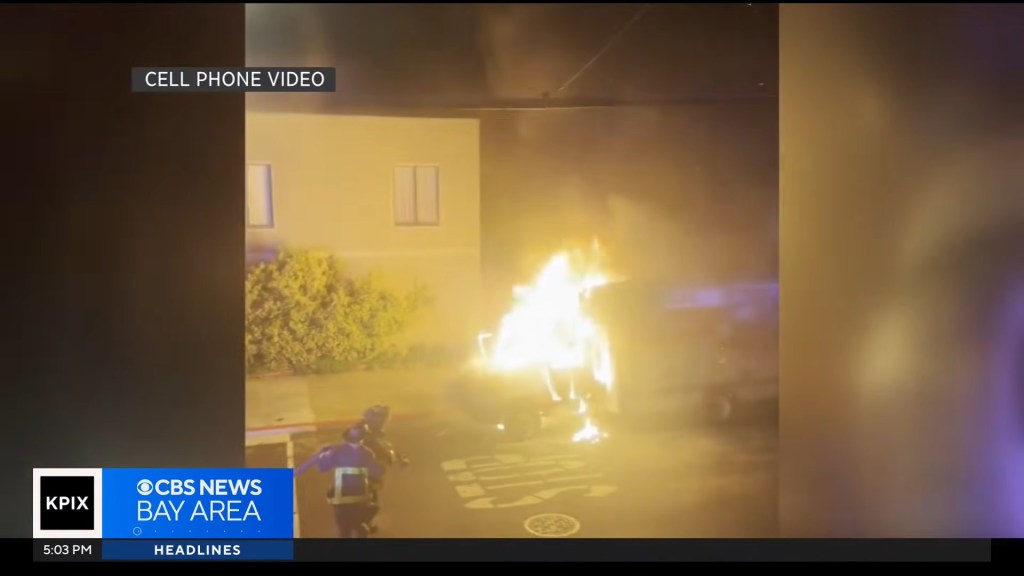 Cell phone video showing a vehicle engulfed in flames with firefighters nearby, during a sideshow.