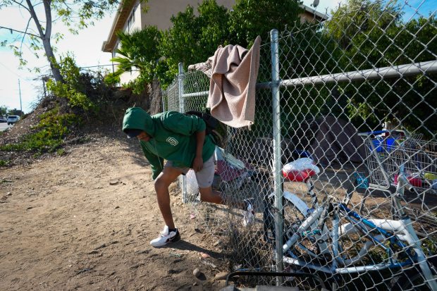 Lemon Grove, CA - November 12: Dalen Harrison, 30, leaves the encampment through a cut hole in the fence where he has lived for the past 2 months in Lemon Grove. (Nelvin C. Cepeda / The San Diego Union-Tribune)
