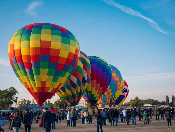 Crowd watching rainbow colored hot air balloons ready for flight
