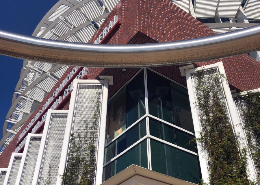 Modern building with a red brick facade, large glass windows, vertical greenery panels, and a curved metal structure in the foreground.