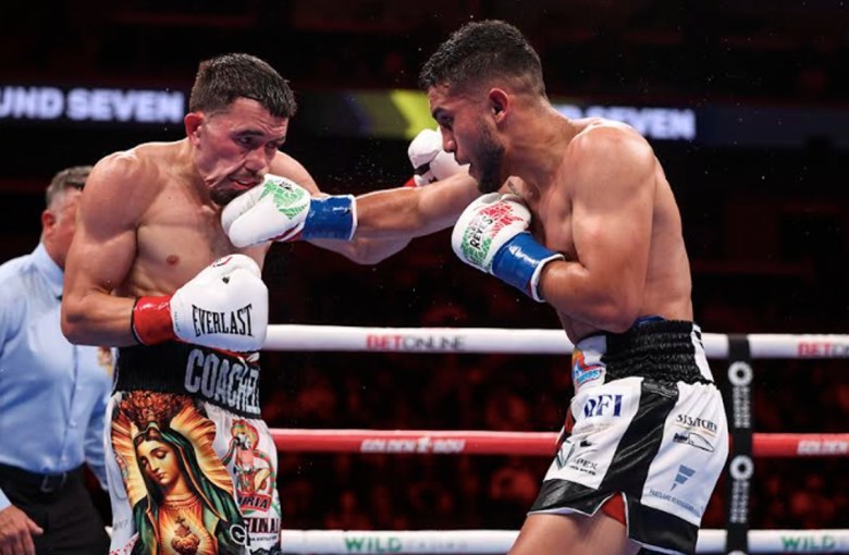 In the ring, one boxer extends his right arm, landing a punishing punch to the left side of his opponent's face.