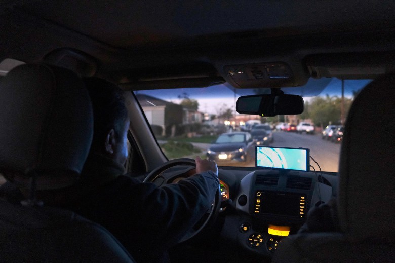 A person drives a car through a residential street as a GPS monitor on the dashboard notes their location.