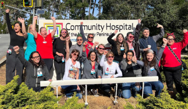 Group of nurses in front of hospital smiling, with raised fists