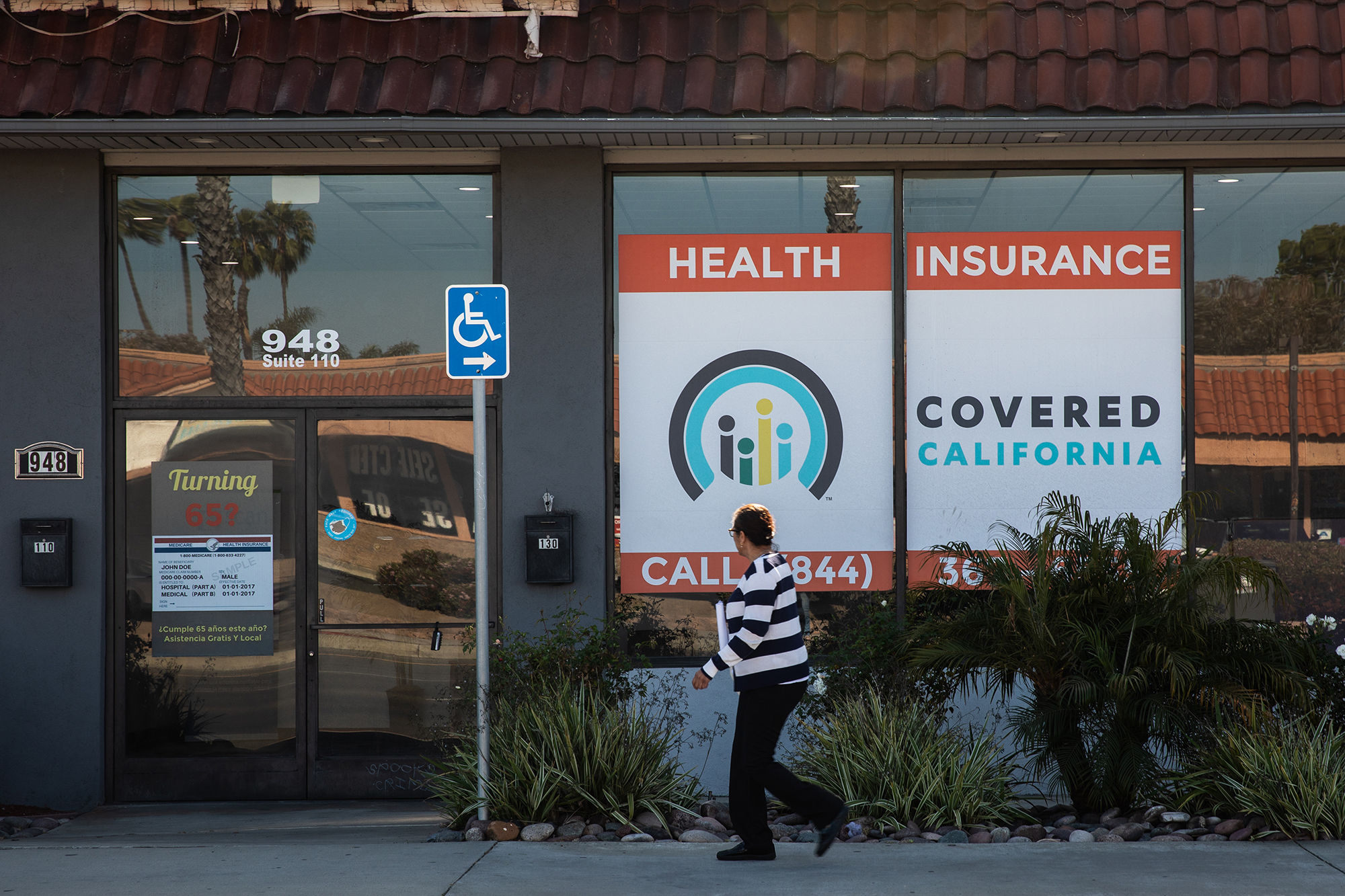 A woman wearing a black and white striped shirt walks past a building with a sign that says 