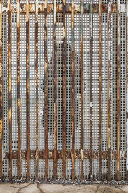 Rusty vertical metal bars with a grid pattern and signs of corrosion stand on a weathered concrete surface.