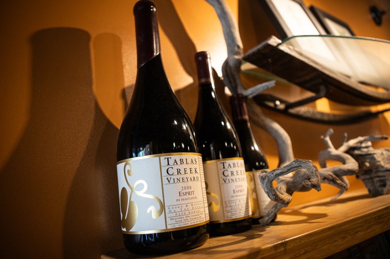 Two bottles of wine sit on a shelf next to some decorative items. The label on the bottle reads "Tablas Creek Vineyard" and "2008 Esprit De Beaucastel"