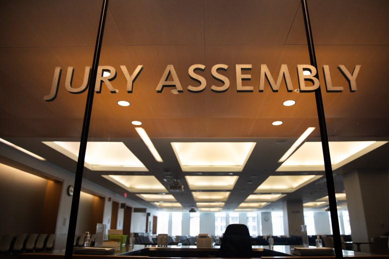 The words "jury assembly" can be seen on the glass window that overlooks an area where jurors gather at a courthouse.