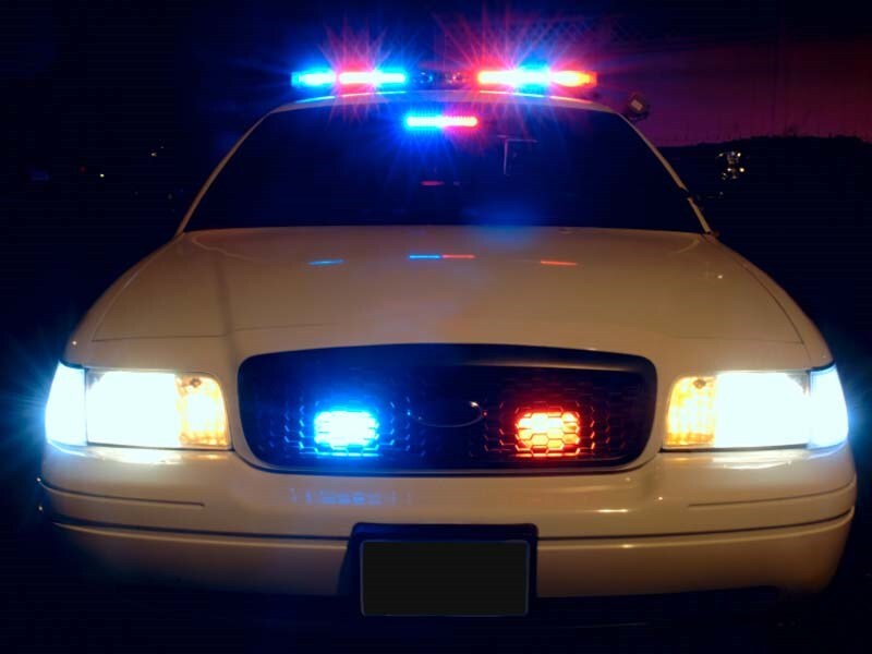 A white police car flashes white and blue lights at night.