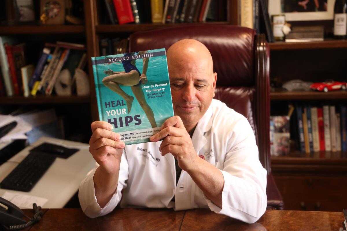 A man seated at a desk holds up a book.