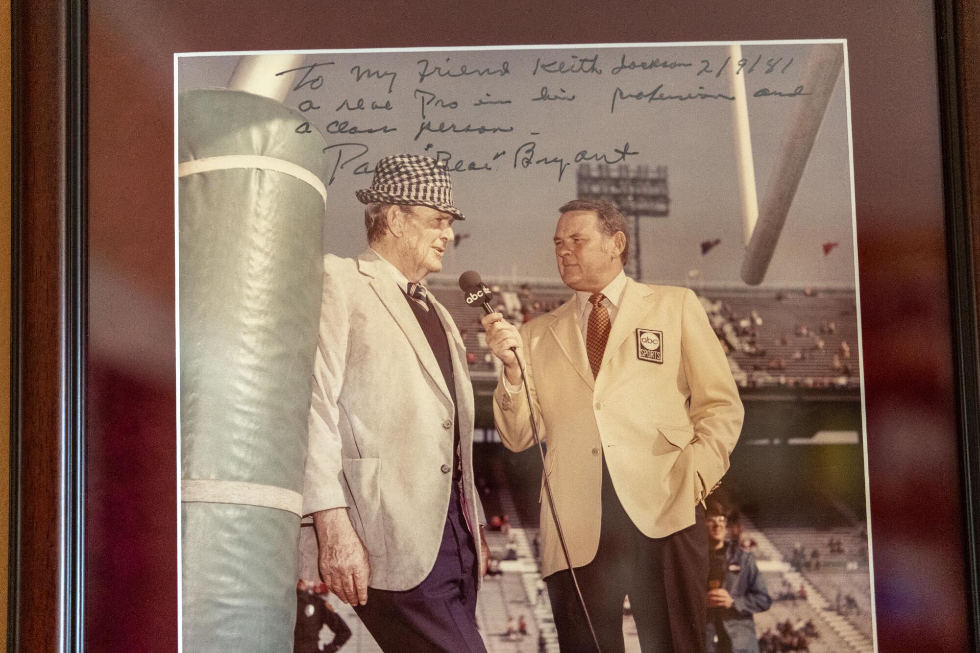 In a framed and signed photo, Keith Jackson interviews famed Alabama coach Paul "Bear" Bryant.