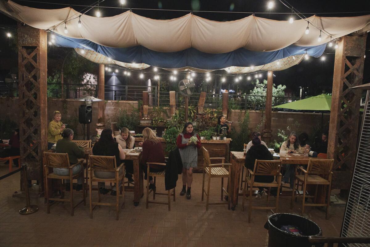A woman walks around the tables showing off a plant on a crowded patio.