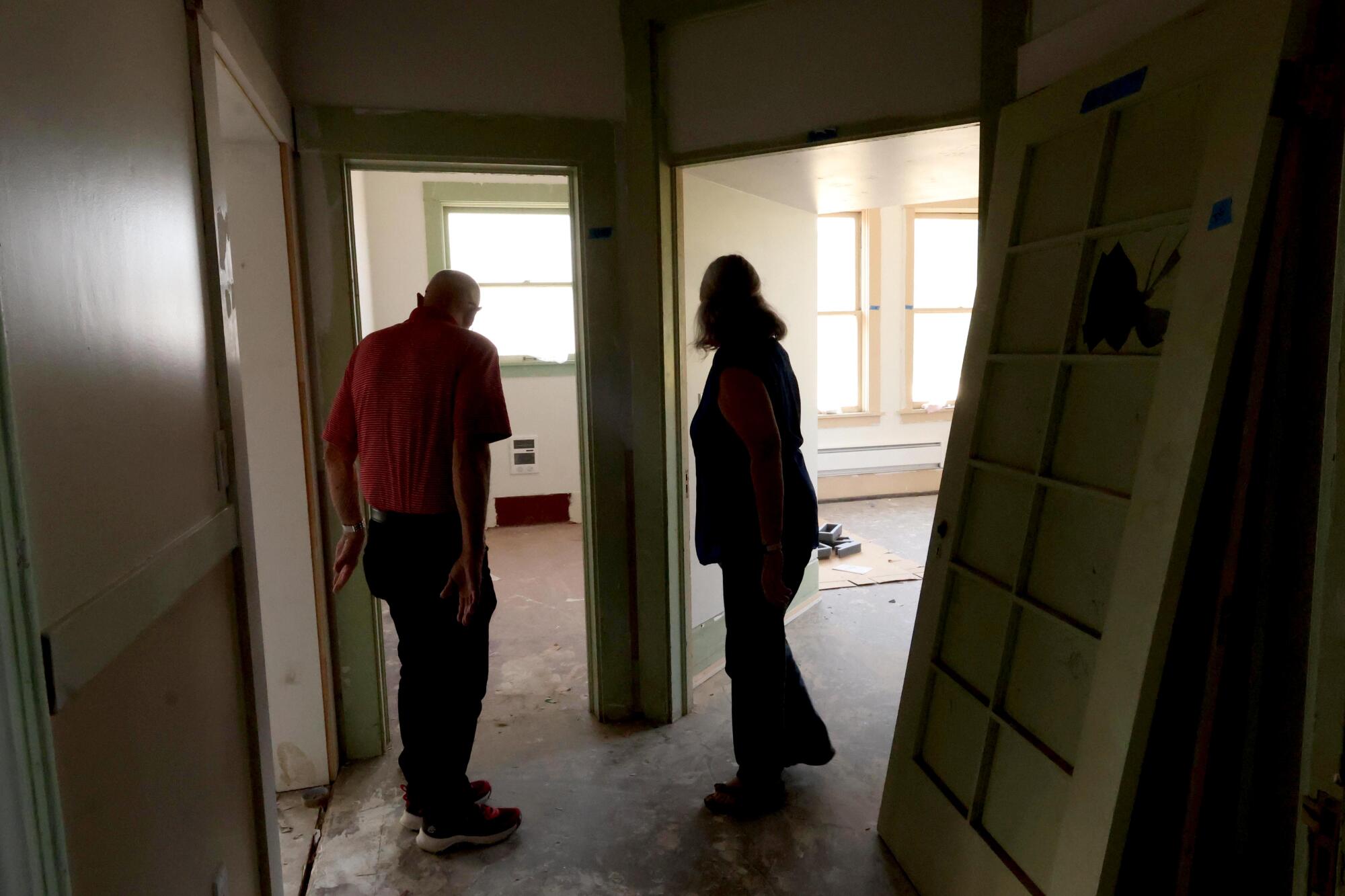 two people look through doorways of rooms being converted into apartments