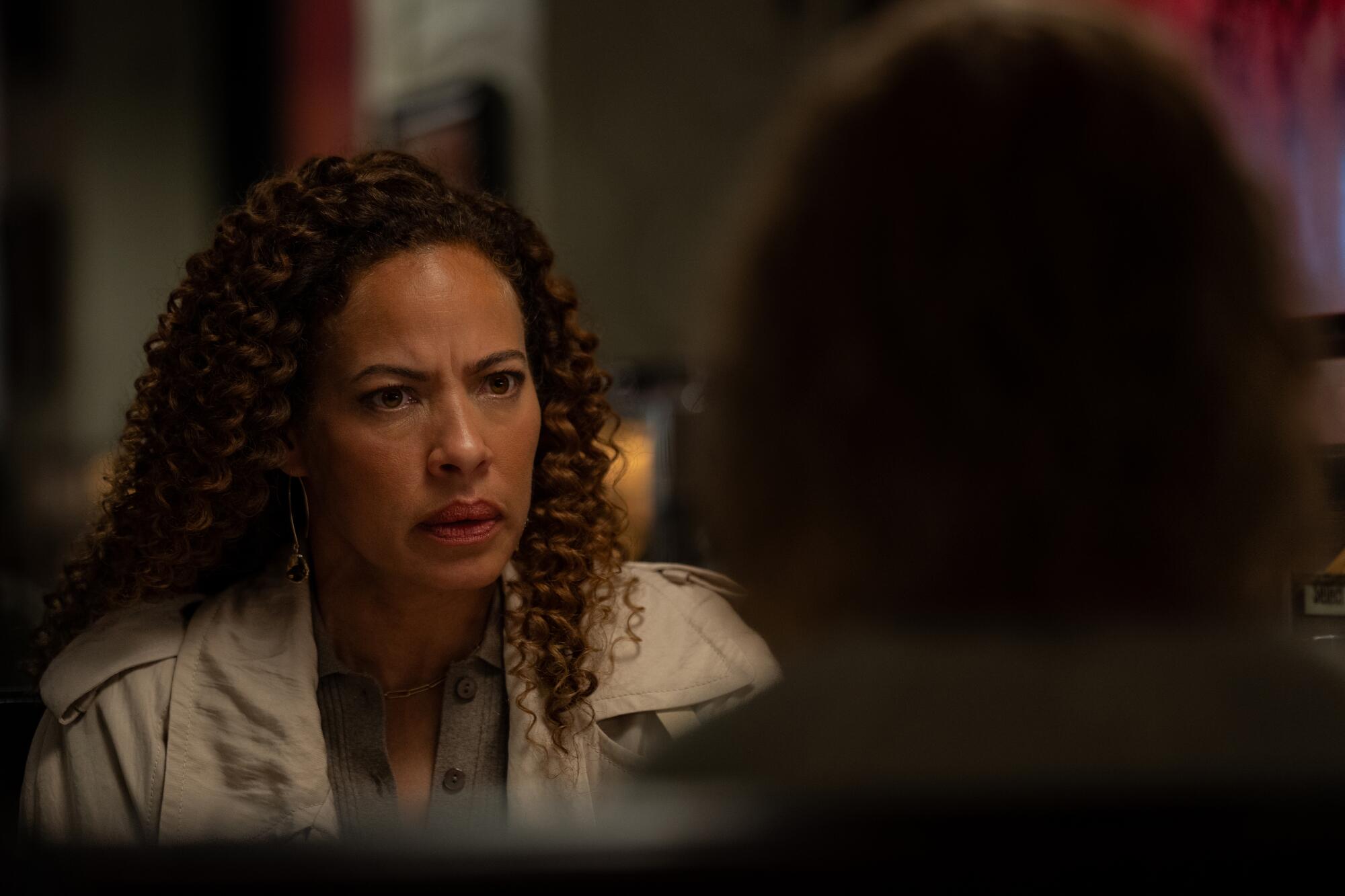A woman with dark curly hair looks intently at another woman, seen from behind, sitting in front of her.