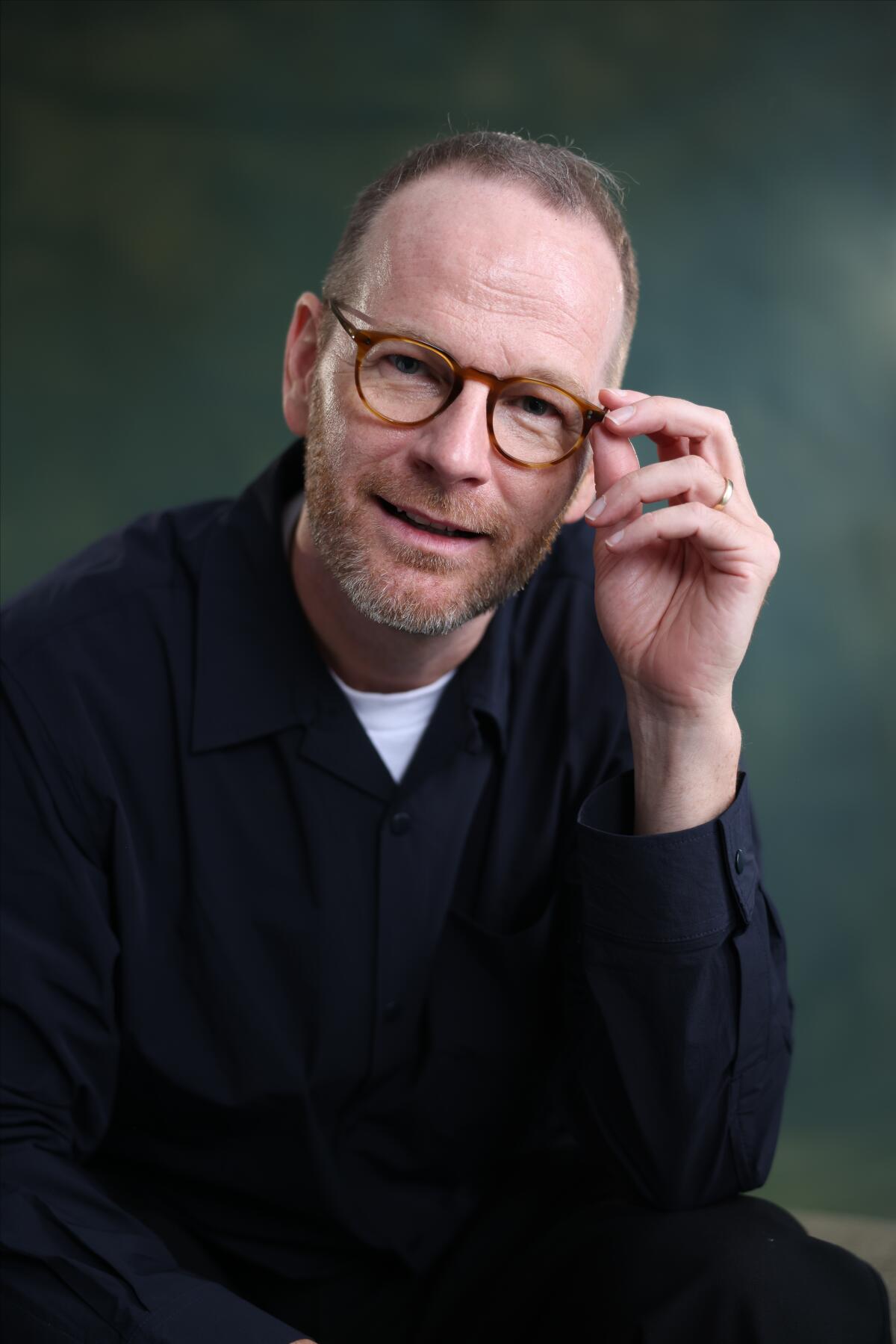 A director wearing eyeglasses smiles.