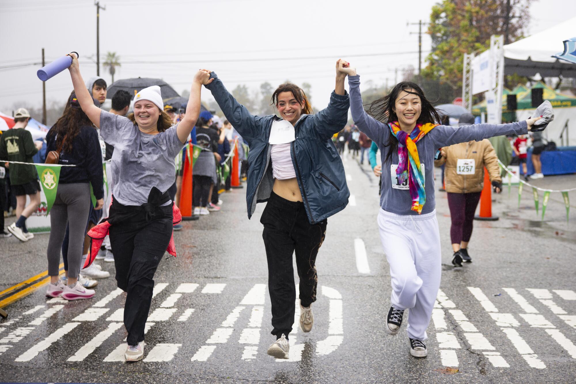 Three people hold their raised hands as they cross a finish line.