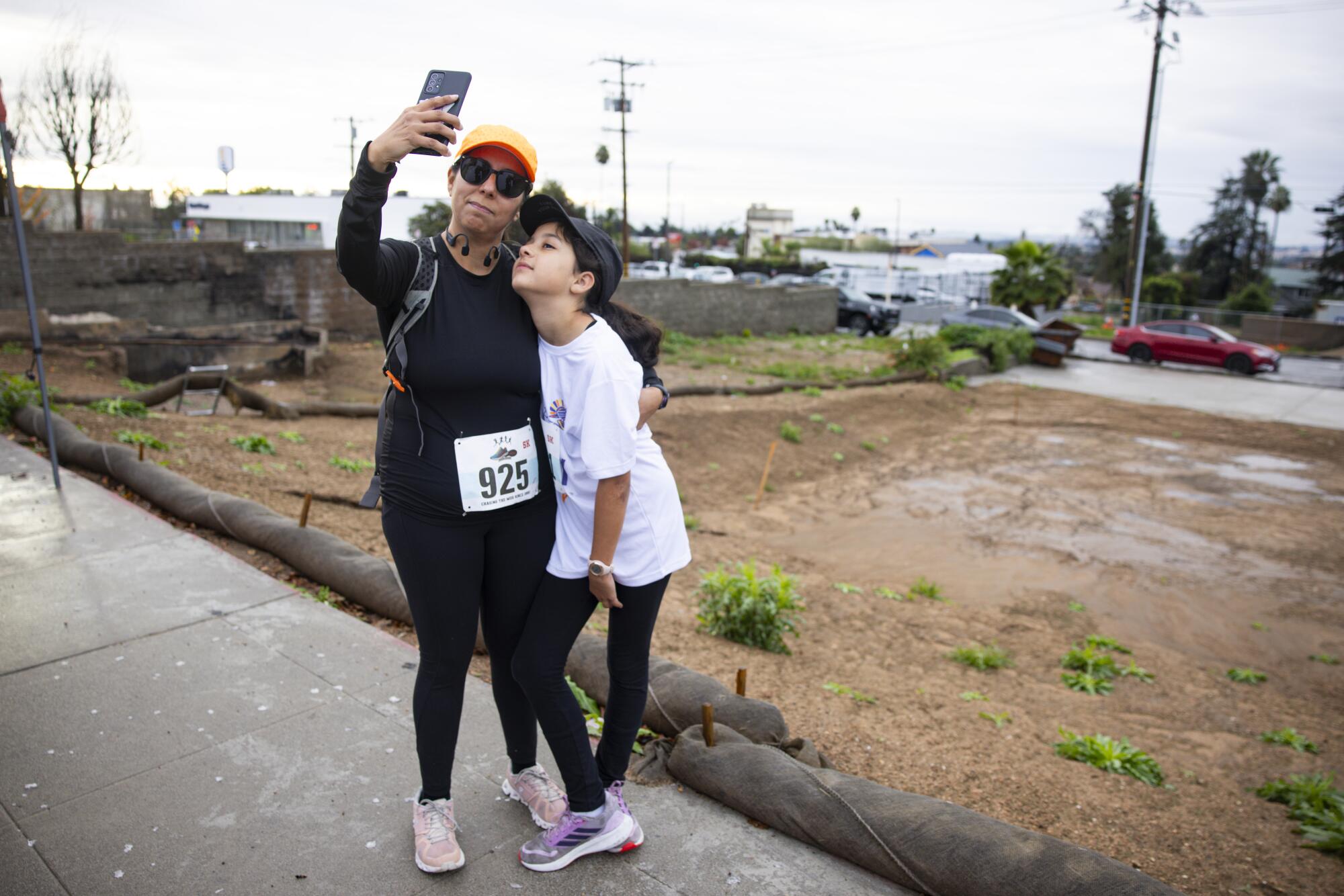 A woman and her daughter take a selfie next to an empty lot.