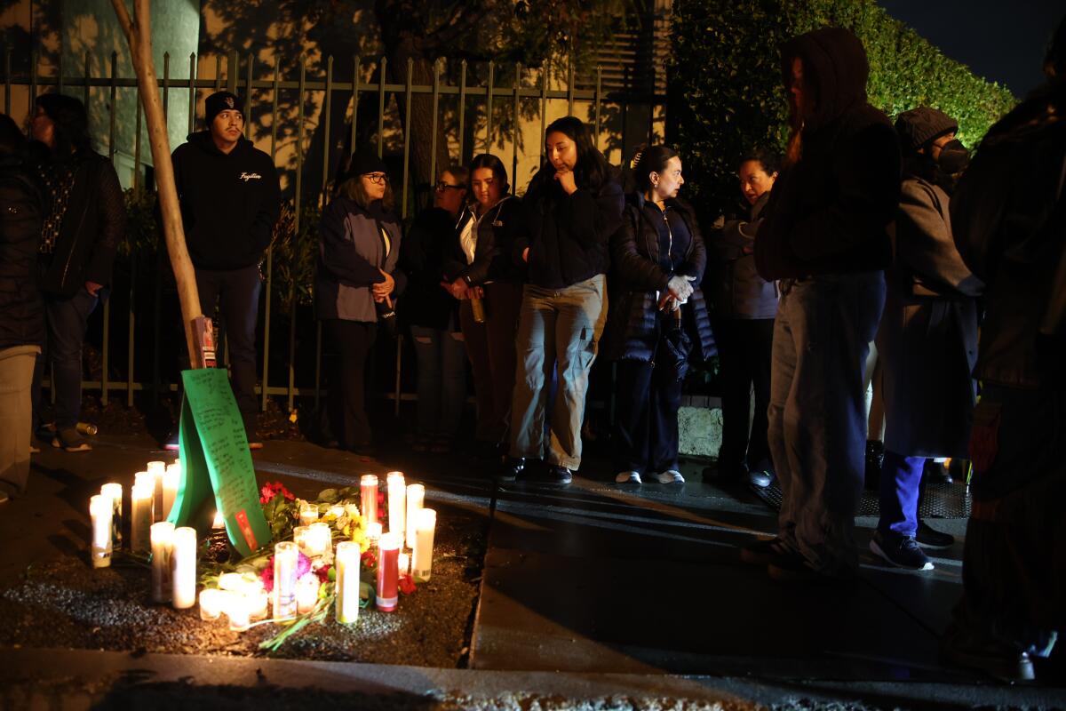 People stand near a makeshift sidewalk memorial full of candles in the evening.