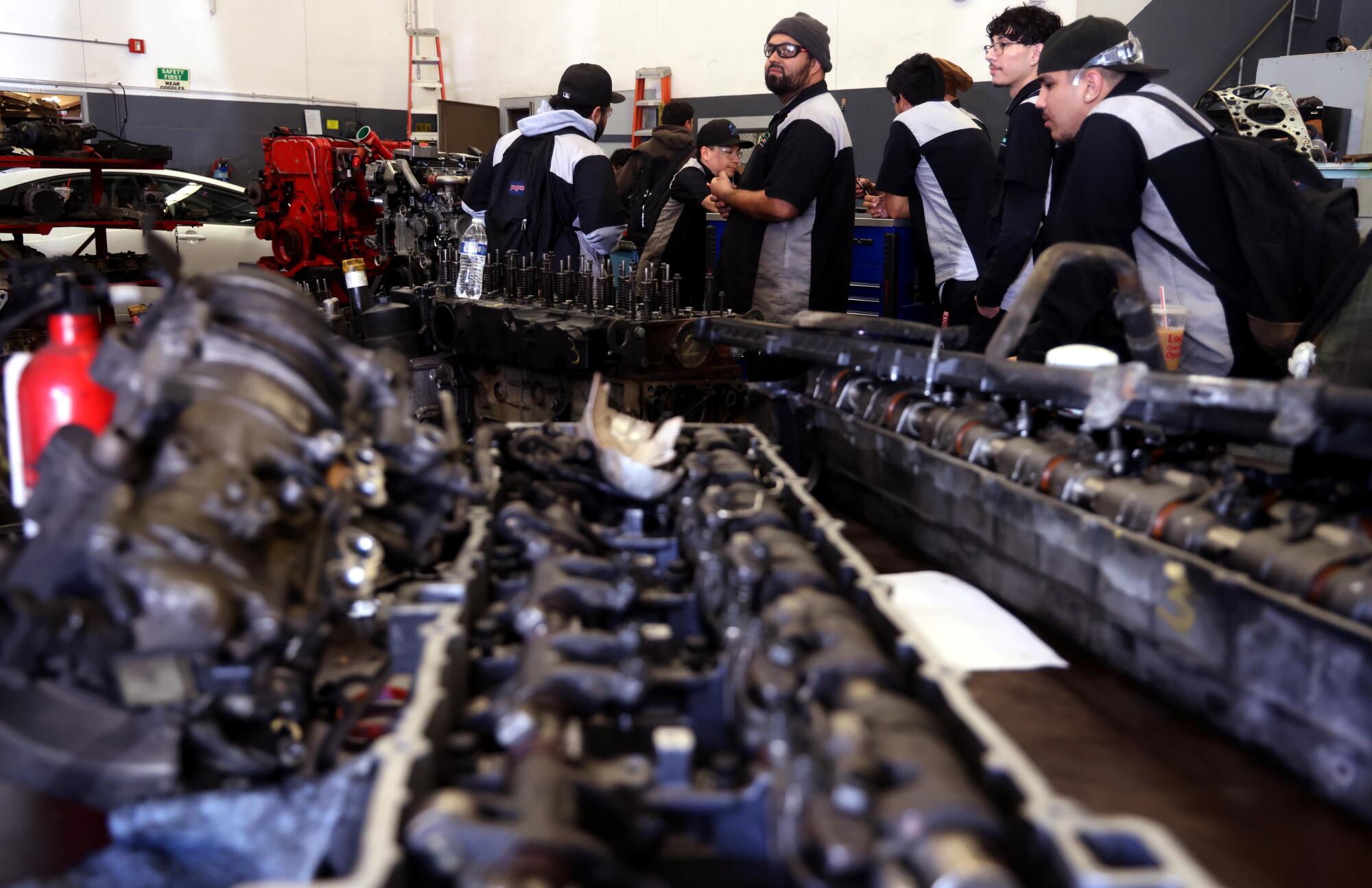 Students stand behind rows of car engines.