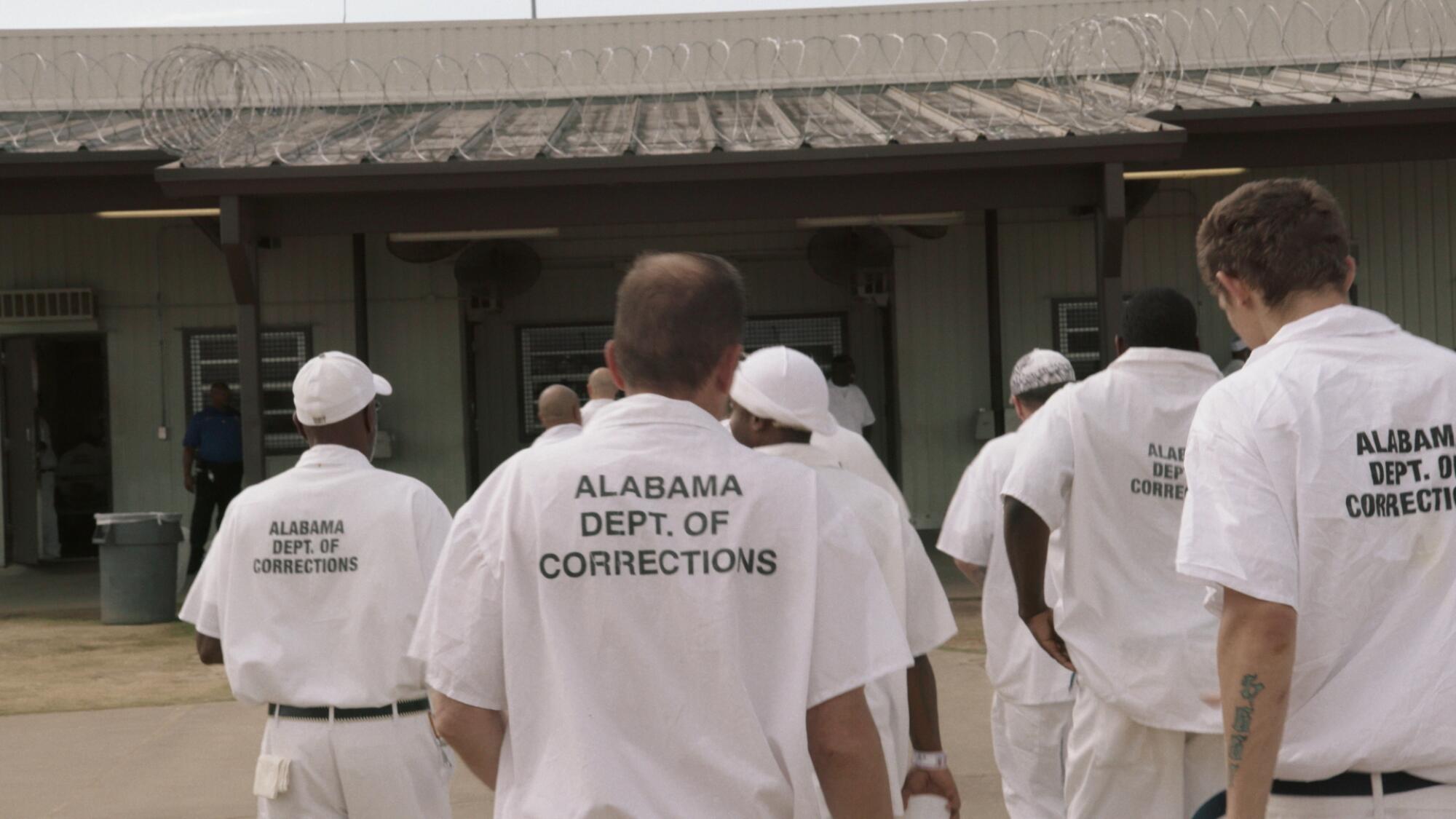 Inmates stand in the yard of a correctional facility.
