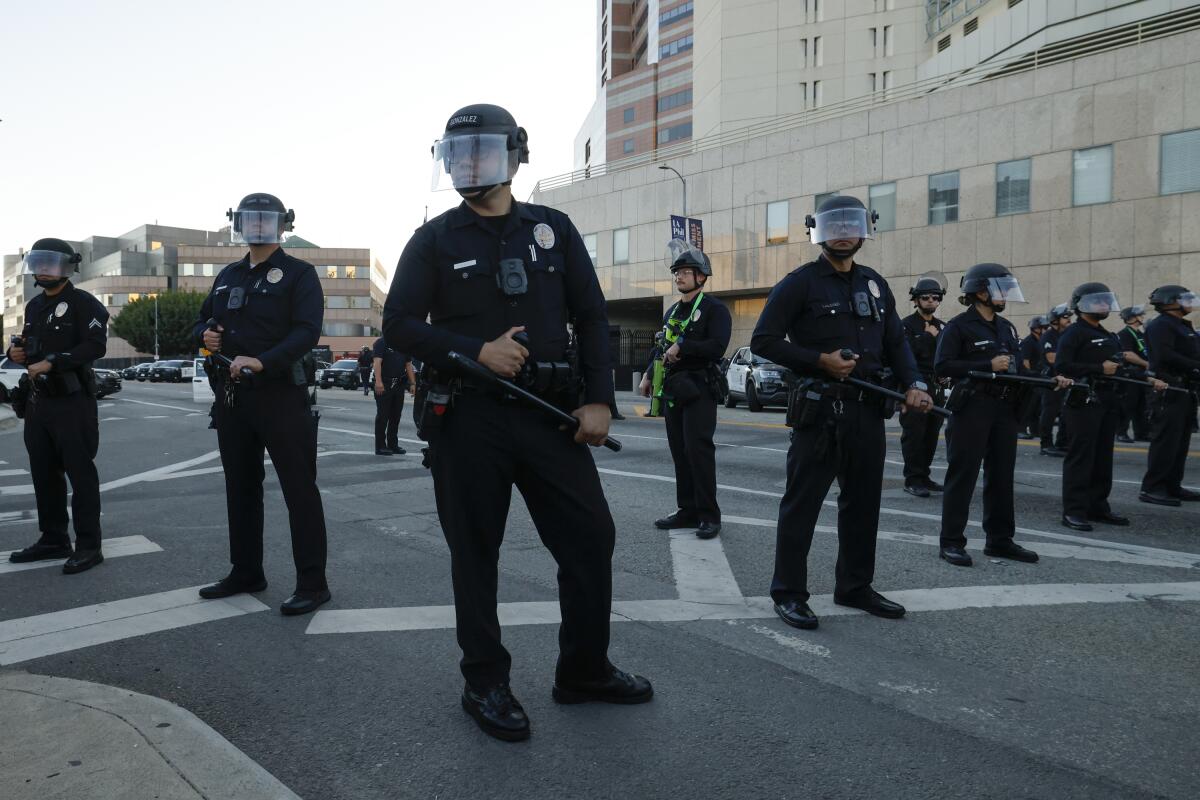 Police officers in face shields stand in the street.