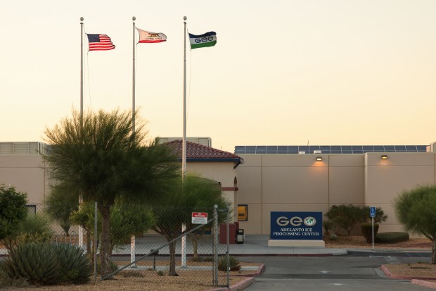 The GEO Group Inc. logo is displayed on a flag alongside the United States and California flags outside the Adelanto ICE Processing Center and detention facility on July 10, 2025. (Photo by Patrick T. Fallon / AFP via Getty Images) 
