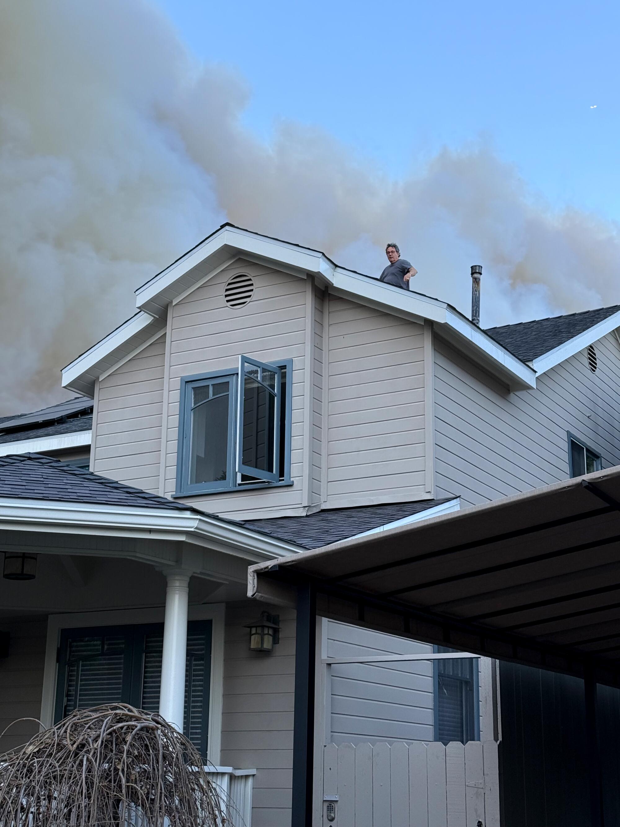 A man seen on a rooftop from a distance as smoke clouds billow above.