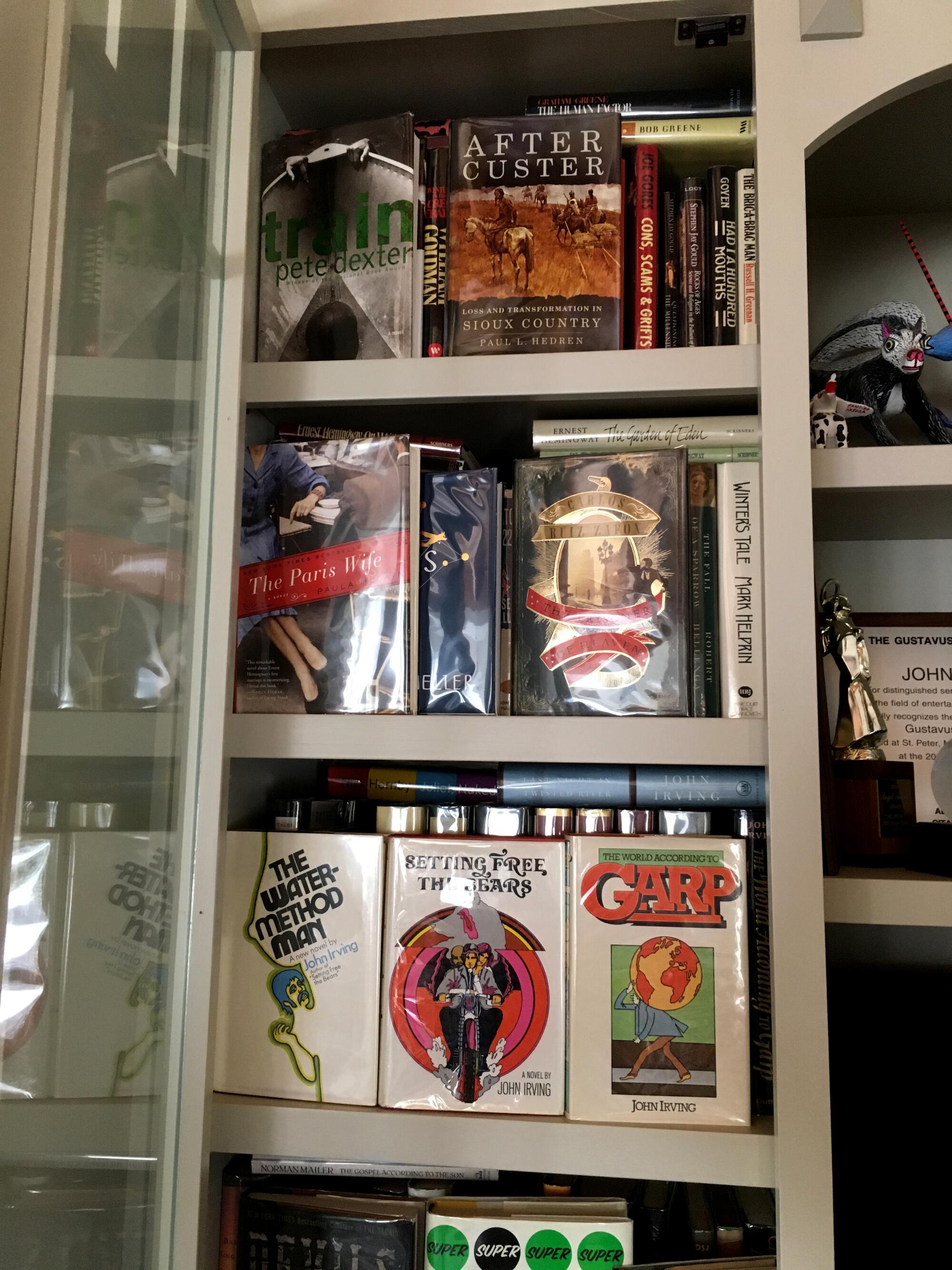 A closeup of a book shelf lined with books, with the covers of several John Irving novels turned forward.