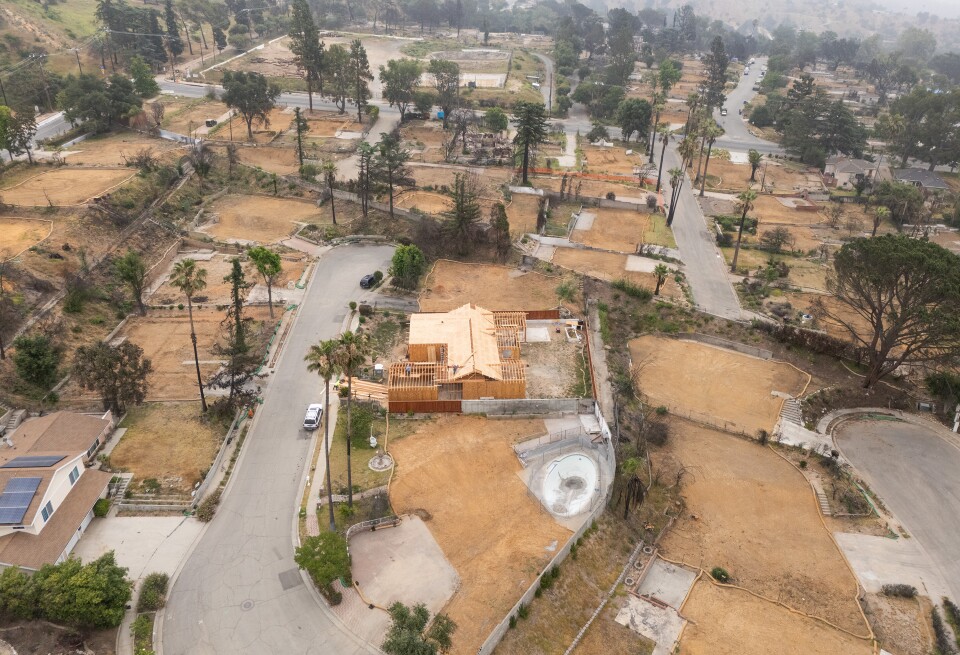 A partially built wooden structure stands among empty dirt lots. A few trees are peppered between the property lines. 