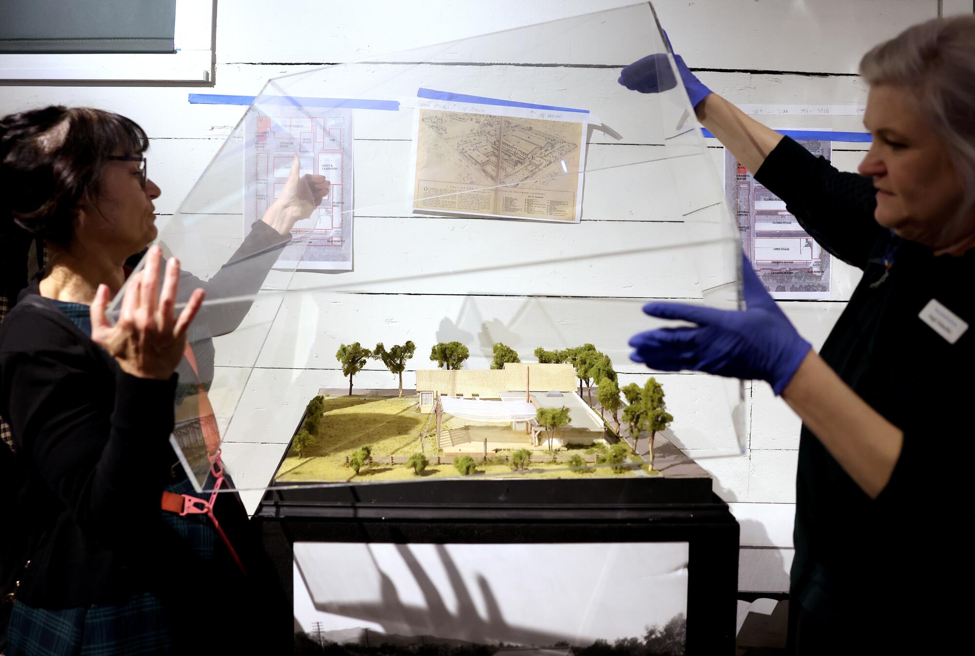 Margot Gerber and Angie Schneider lift up plexiglass above a miniature display.