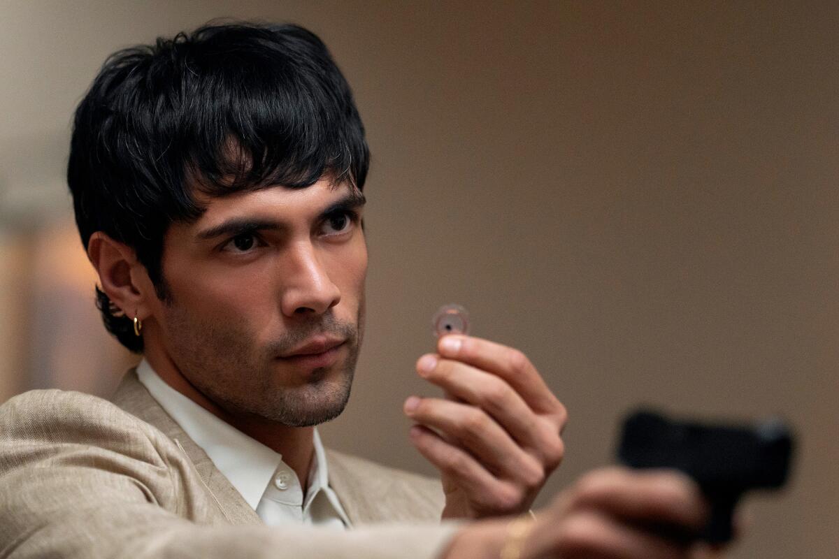 A man holds up a tiny device held between his fingers while raising a handgun. 