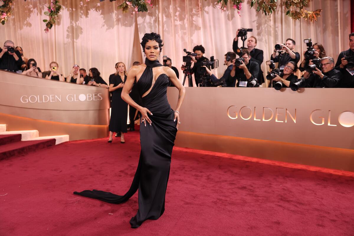 Teyana Taylor poses on a red carpet in a black halter gown with a train.
