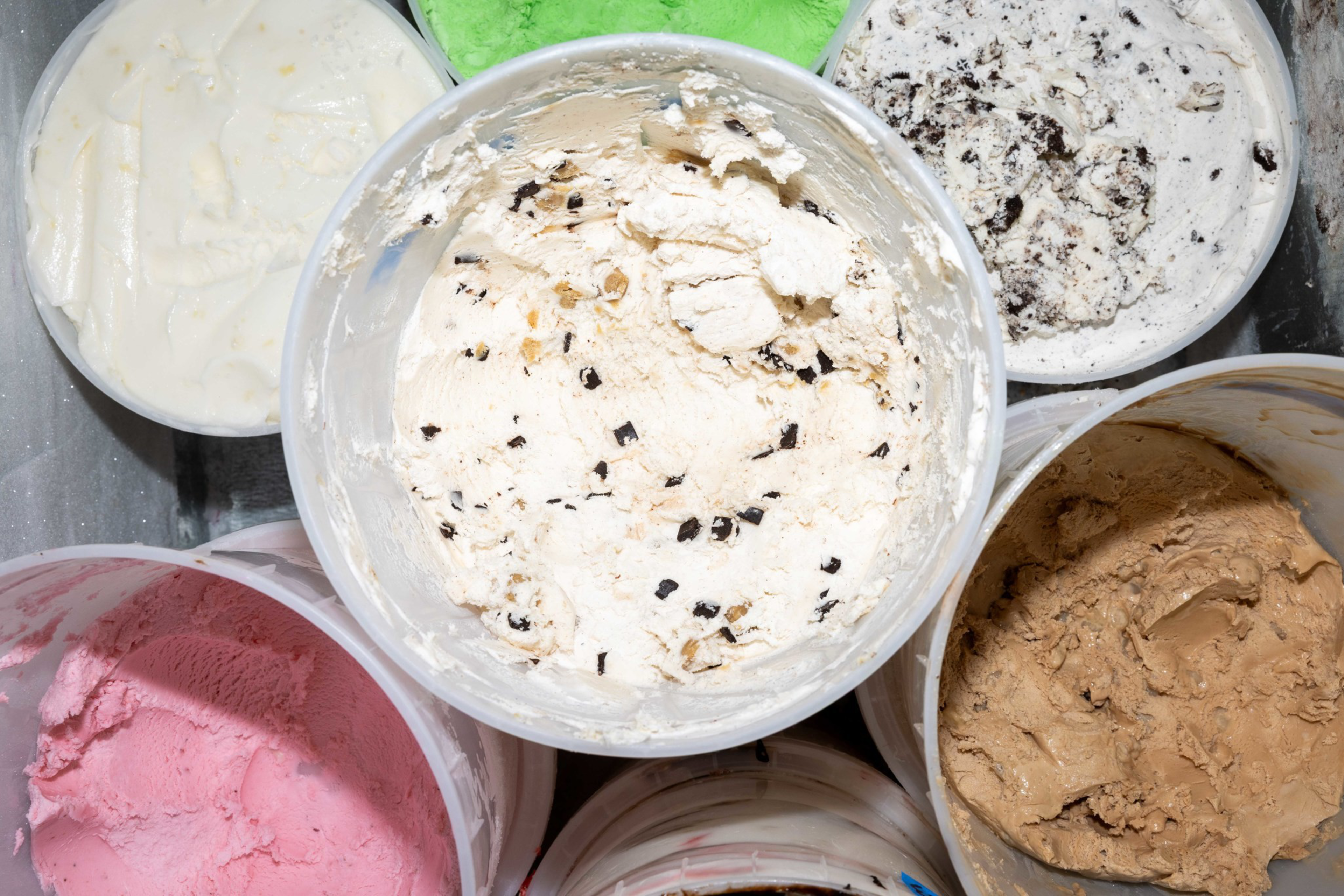 Multiple tubs of ice cream in various flavors including chocolate chip, mint, strawberry, coffee, vanilla, and cookies and cream.