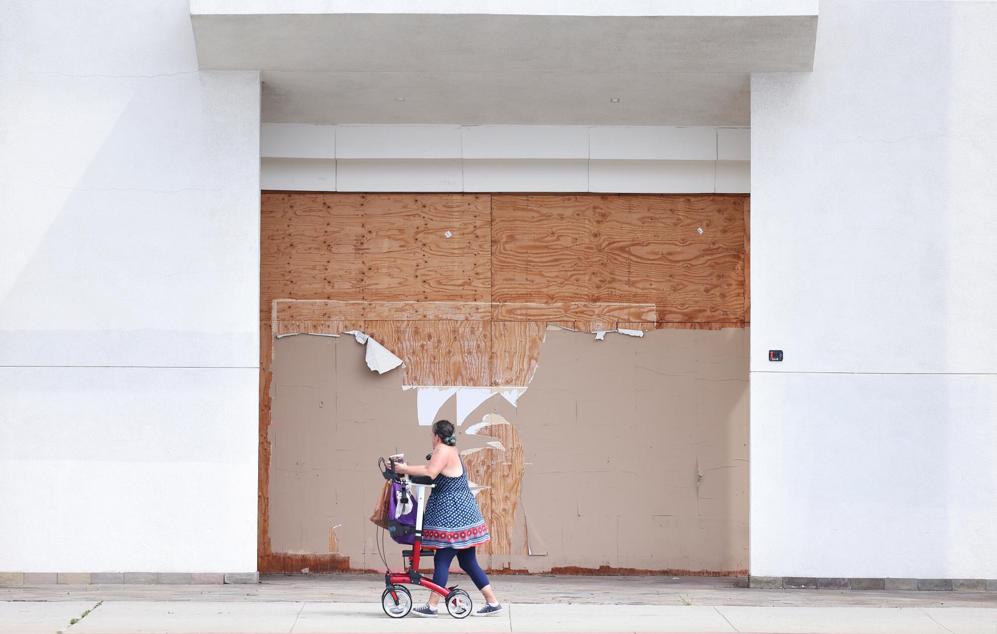 A pedestrian walking past a closed storefront sealed off with wooden boards