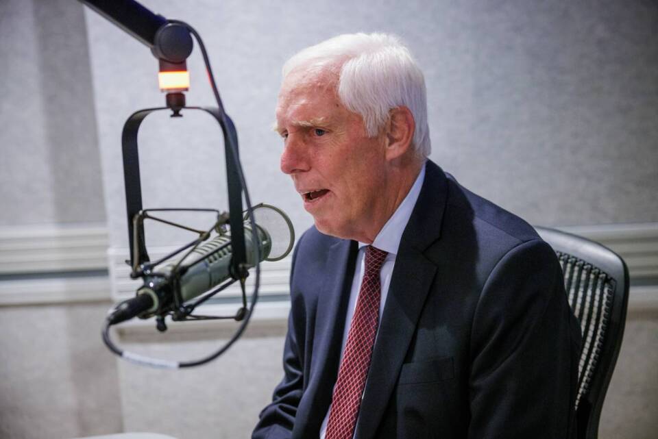 Stephen Wagstaffe, a man with light skin tone and white hair who is wearing a dark suit and red striped tie, speaks into a microphone in a studio.