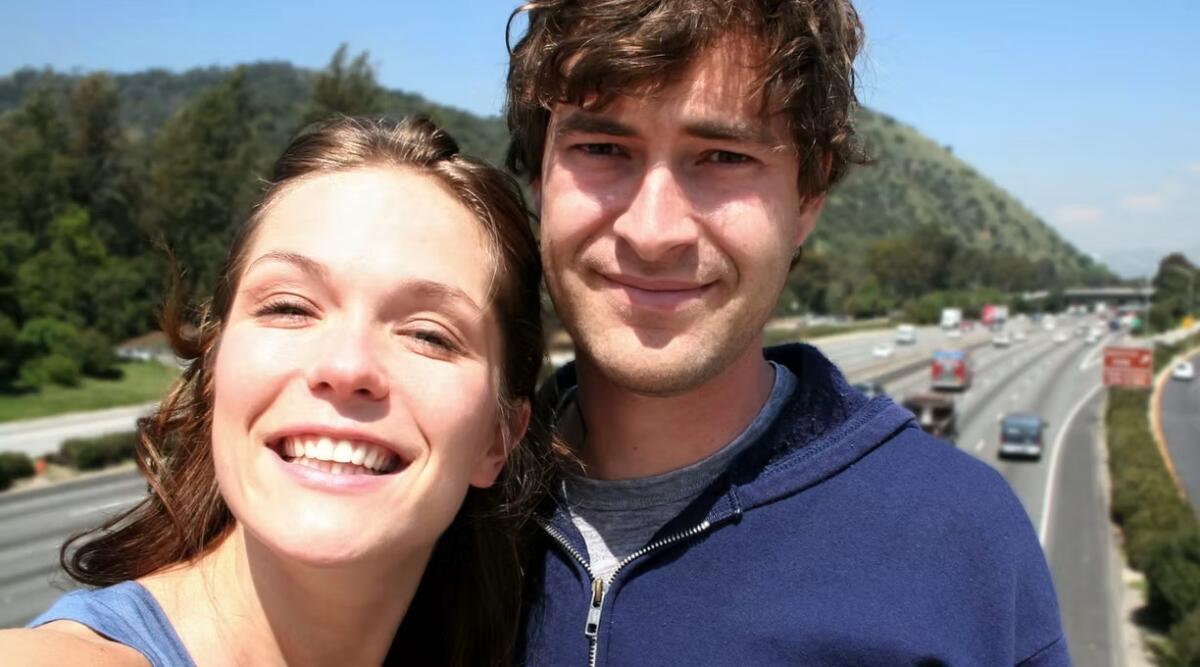 Two people smile and pose in front of a road.