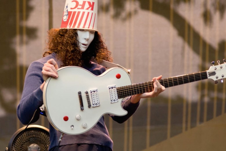 Man wearing KFC bucket on head and white mask, holding electric guitar