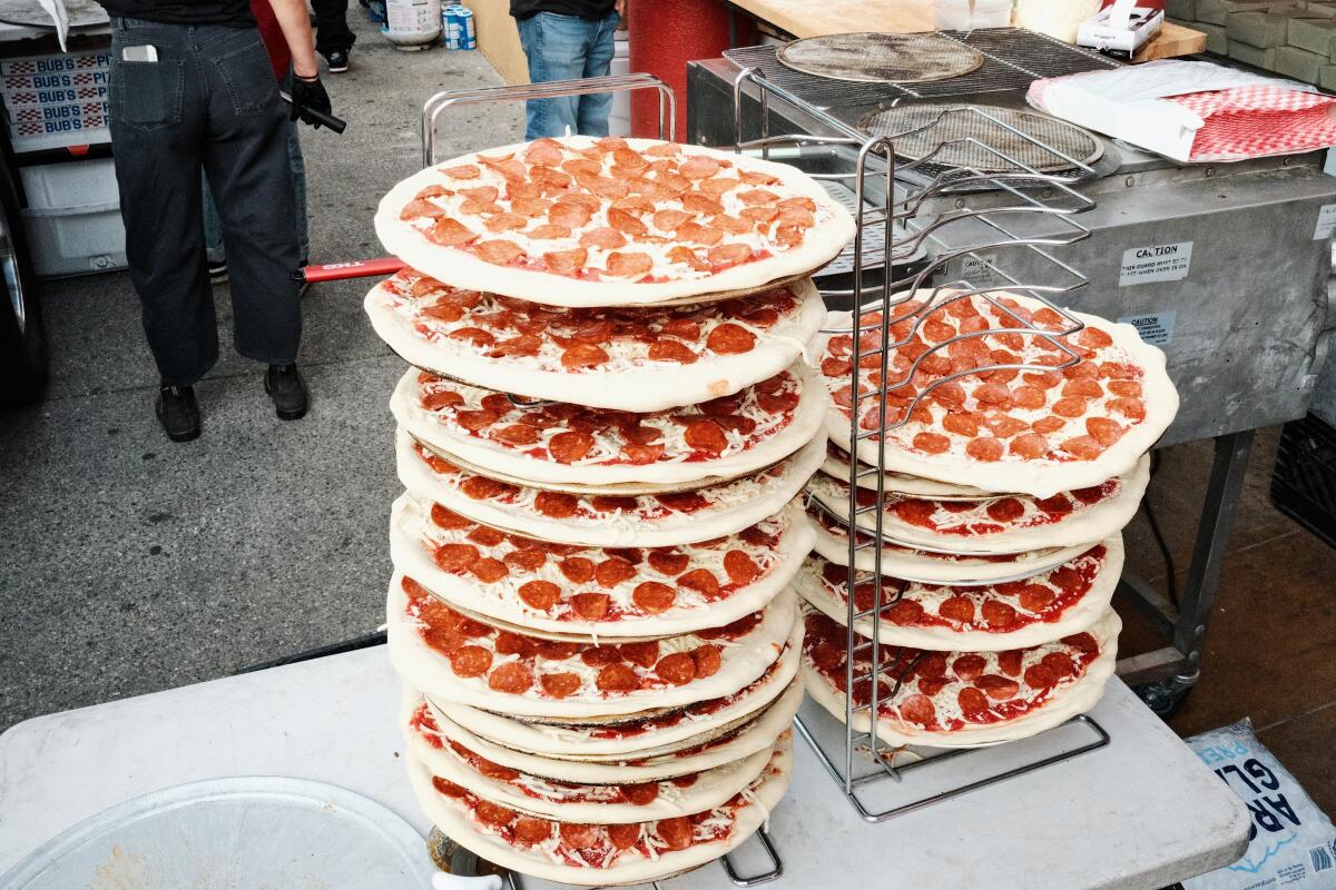 Two stacked towers of pepperoni pizza ready for the oven outside a restaurant