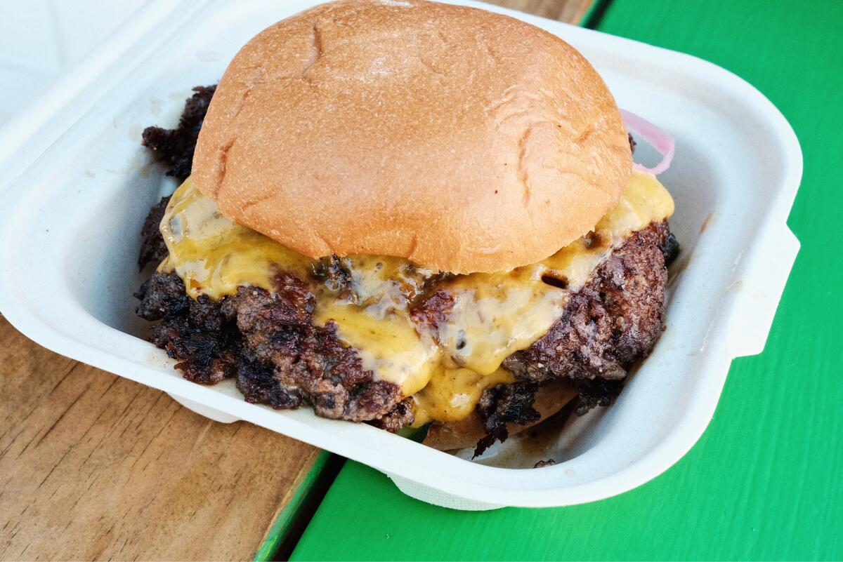 A double cheeseburger in a to-go paper tray on a green and brown wood table