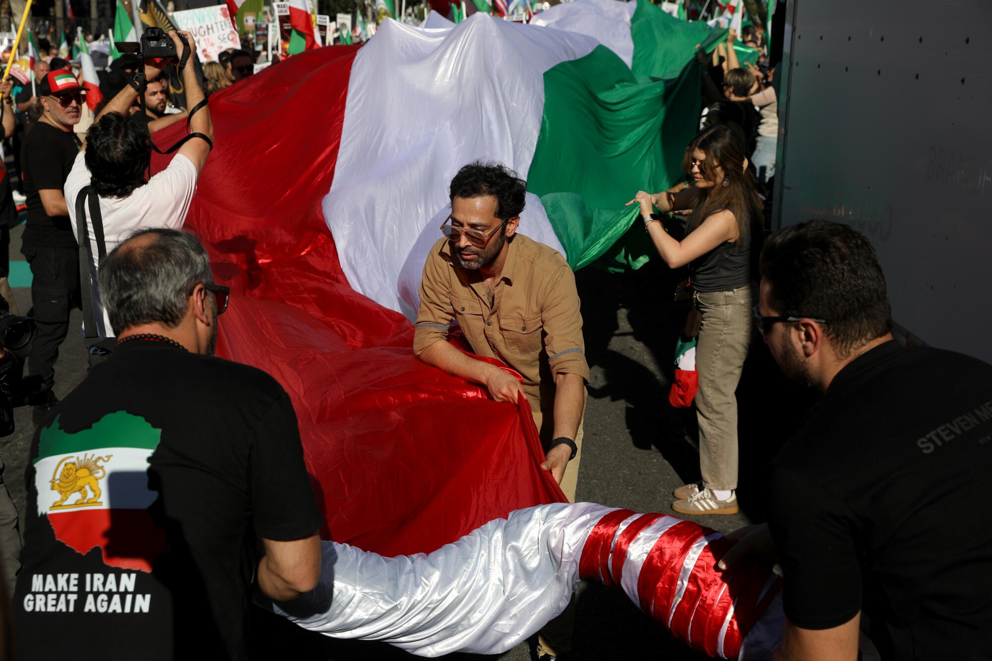 People unravel an Iranian Pre-Revolutionary flag as Iranians gather for a Make Iran Great Again march / rally.