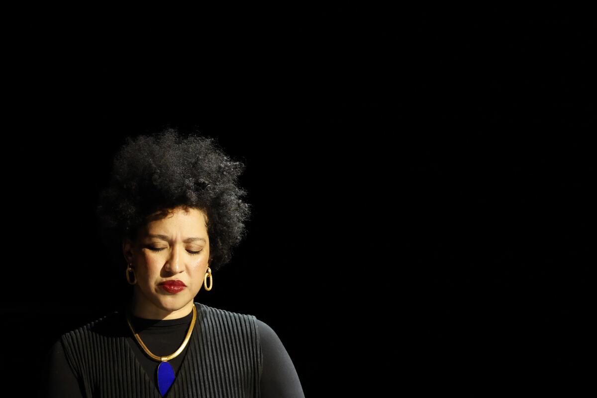  Julia Bullock in a black top with a gold and blue necklace in front of a black background