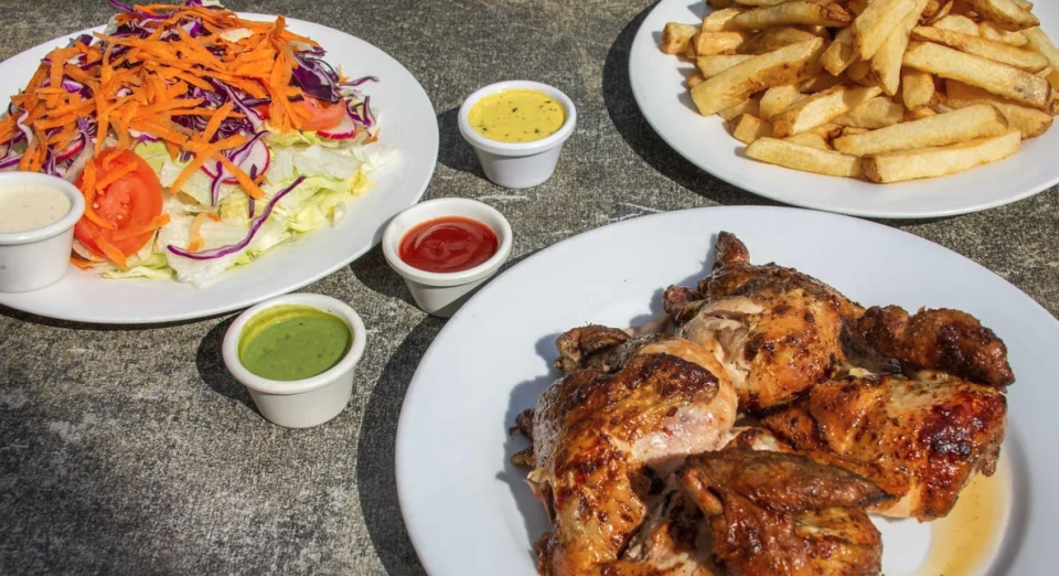 Three white plates sit on a grey marbled table. One contains a green salad topped with orange carrots; another has a pile of french fries, and the third has pieces of juicy chicken