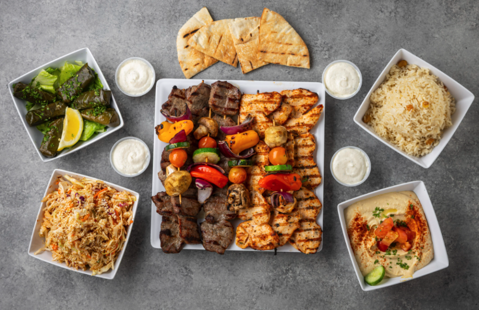 An array of white dishes, containing humus, yellow rice, pita bread, grapeleaf rolls and kebabs of chicken and beef