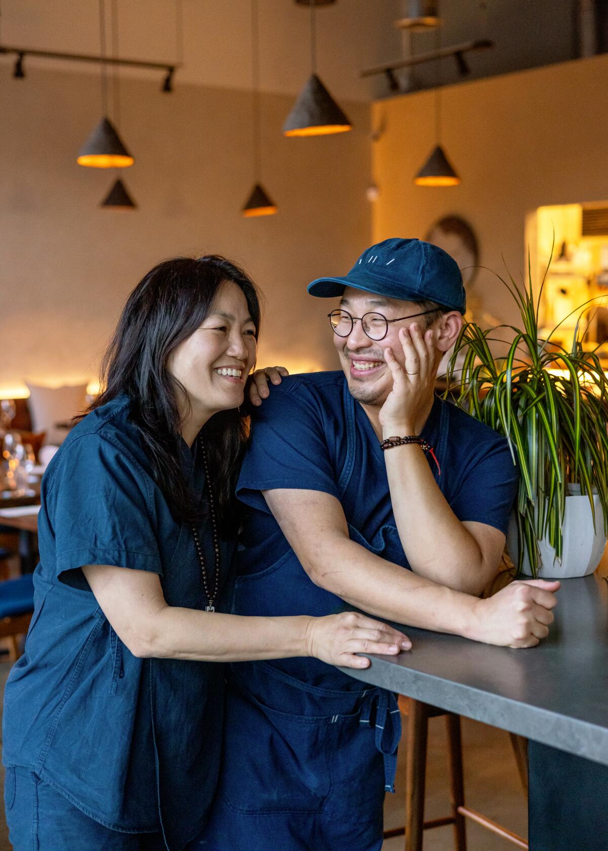 A man and woman stand in a dining room, smiling