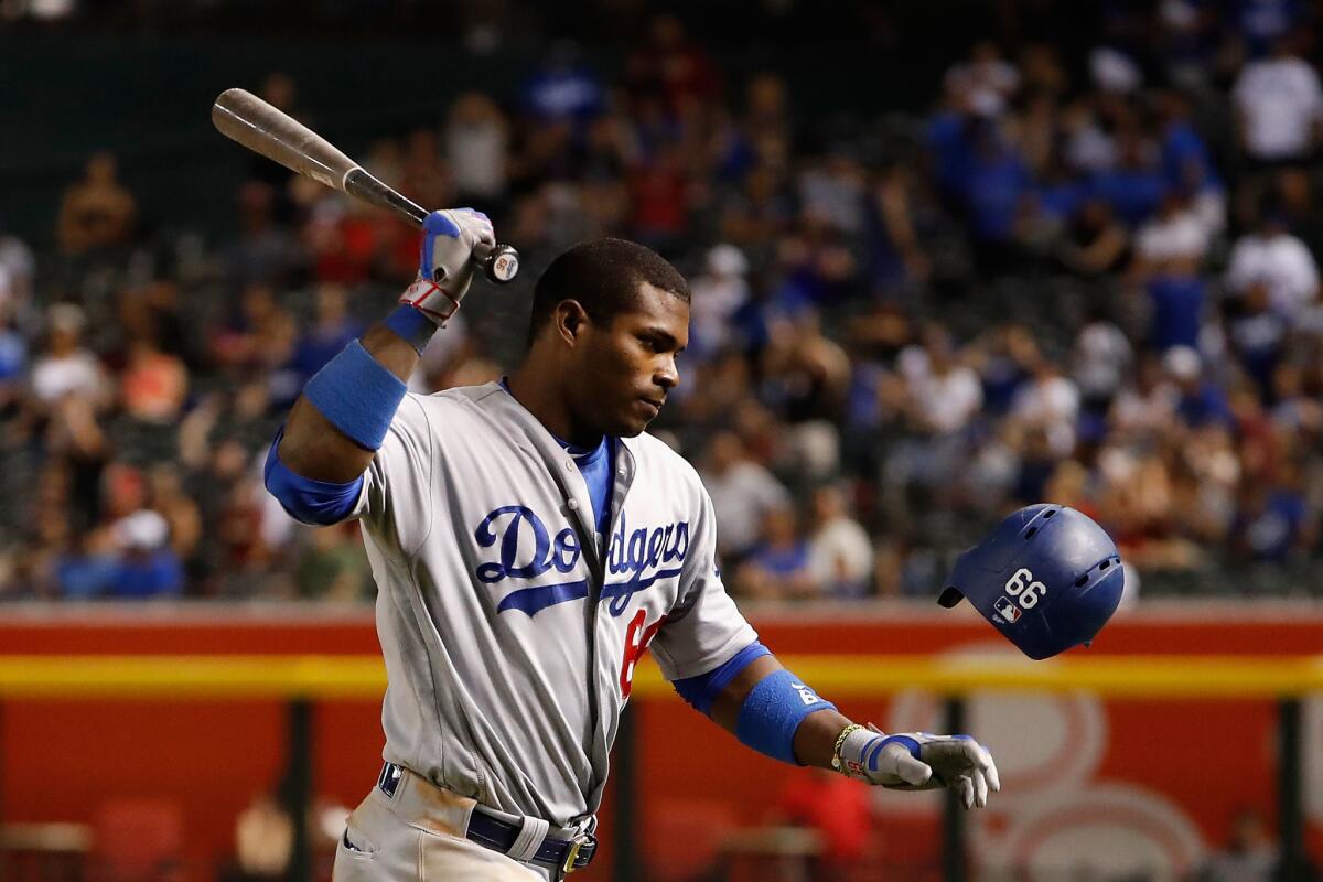 Yasiel Puig swings a bat at a falling helmet while wearing a Dodgers uniform with arm bands and batting gloves