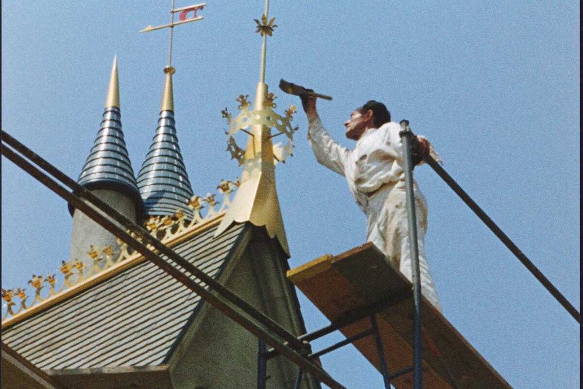 A worker applies gold detailing to the ornate spires of Sleeping Beauty Castle, showcasing the elegance and precision that defined the centerpiece of Disneyland Park.