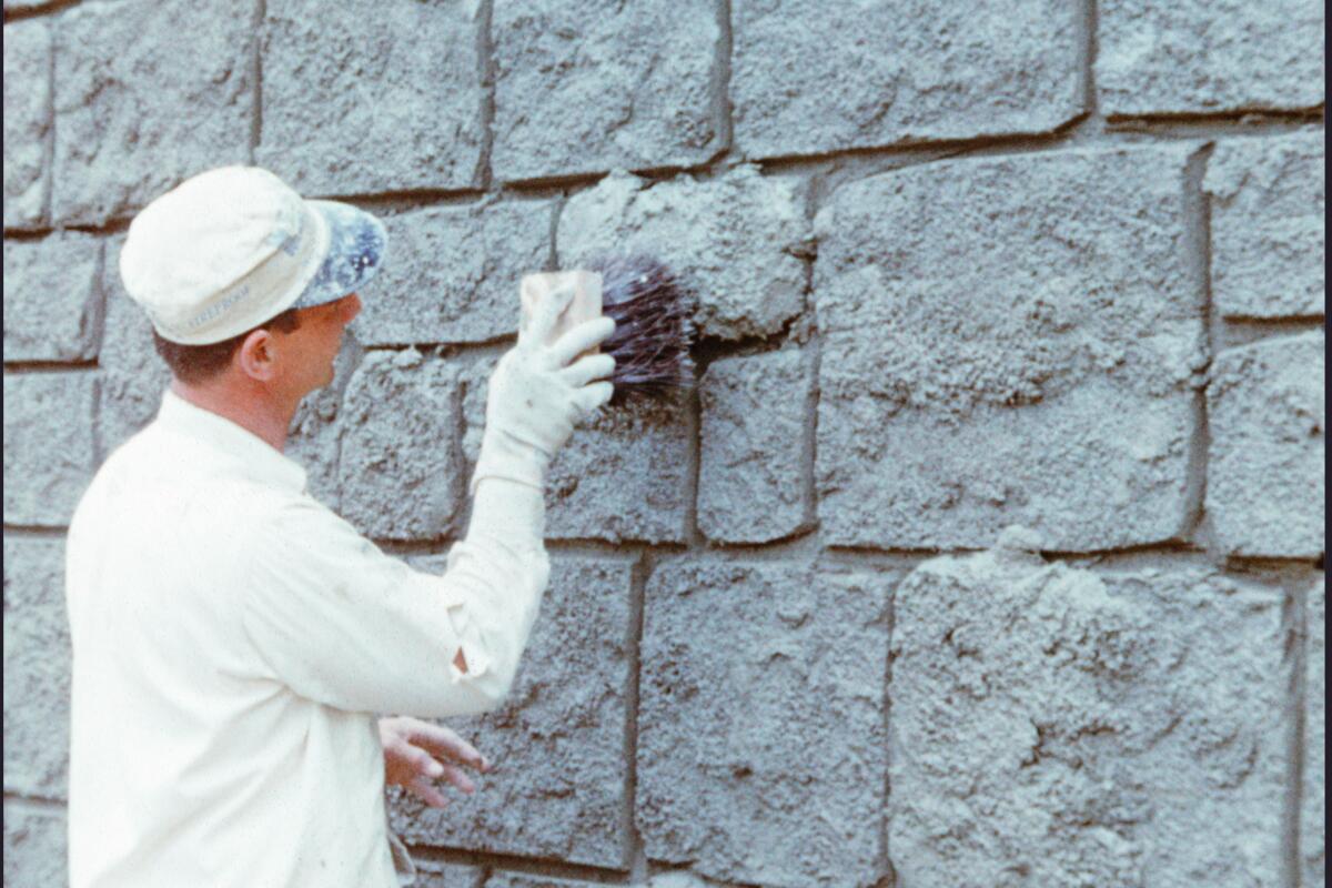 A craftsperson applies paint to the stone facade of Sleeping Beauty Castle.