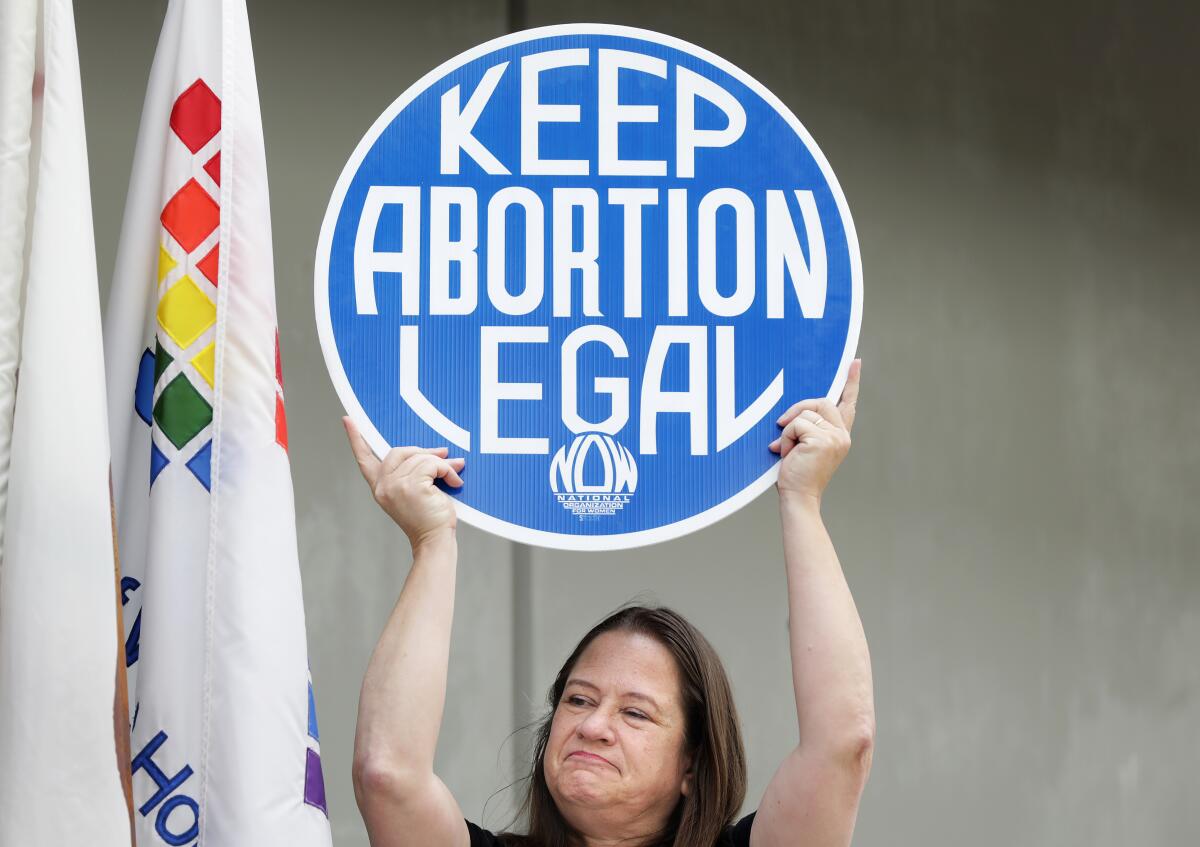 A woman with dark brown hair holds up a large round sign that reads, Keep Abortion Legal
