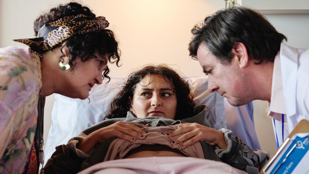 Two concerned adults lean over their daughter in bed.