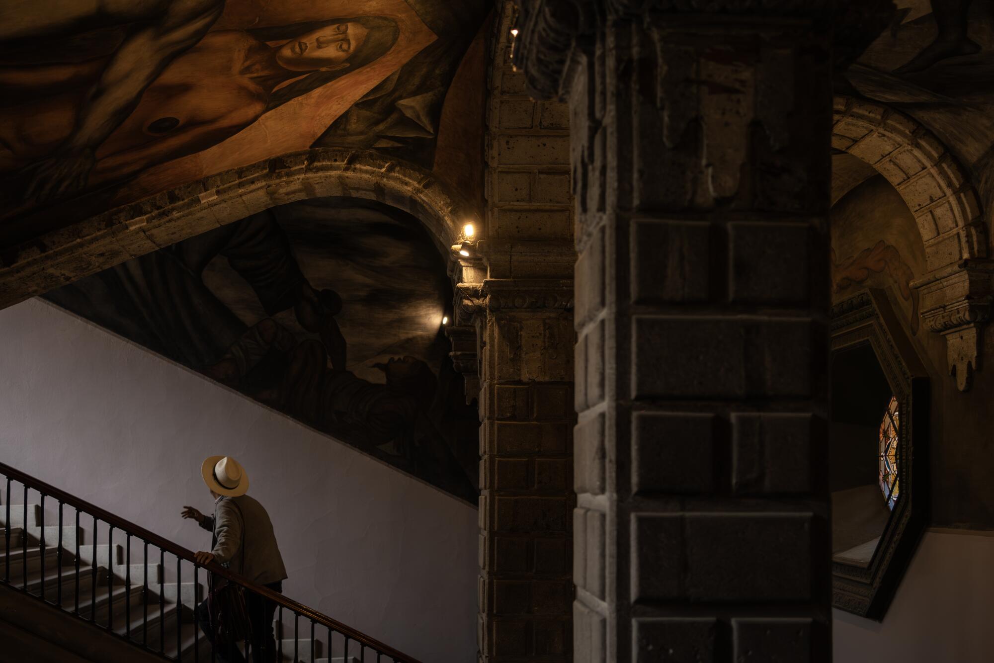 A man ascends the stairs beneath the mural "Cortes y la Malinche"